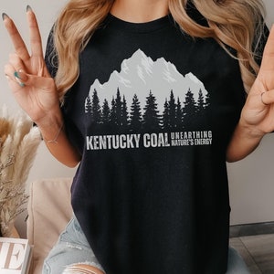 May include: Black t-shirt with a graphic of a mountain range and trees. The text "Kentucky Coal Unearthing Nature's Energy" is printed on the shirt.