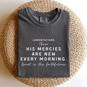 May include: A dark gray t-shirt with white text that reads "Lamentations Three His Mercies Are New Every Morning. Great is thy faithfulness."