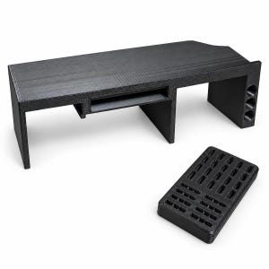 May include: A black monitor stand with a textured surface, featuring a rectangular shelf, a central recessed compartment, and a side panel with three circular cutouts. A separate black rectangular tray with a grid of small slots is positioned nearby.