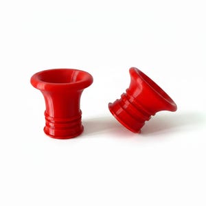 Op de afbeelding: Twee rode flessenstoppers met een uitlopende bovenkant en een geribbelde basis. De stoppers zijn gemaakt van een glad materiaal en zijn ontworpen om in de hals van een fles te passen. De stoppers worden getoond tegen een witte achtergrond.