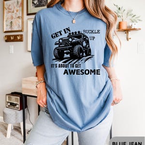 May include: A blue t-shirt with a black graphic of a jeep and the text "Get in... Buckle Up It's About To Get Awesome".