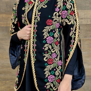 Op de afbeelding: Een zwart geborduurd jasje met een gouden rand en een bloemenpatroon. Het jasje heeft lange mouwen en een ronde hals.