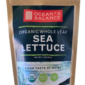 May include: A brown paper bag with a resealable zipper top. The bag contains a 1.5 ounce package of organic whole leaf sea lettuce. The bag has a label with the text "Ocean's Balance", "Organic Whole Leaf Sea Lettuce", "Net Wt. 1.5 oz (42 g)", "Clean Taste of Maine", and "USDA Organic". The label also features a graphic of a boat sailing in a bay.