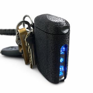 May include: Black key organiser with a textured surface and blue LED lights. Several keys are attached to the organiser. The lights are in the shape of a flower.