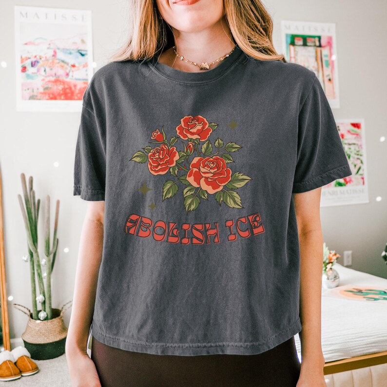 Charcoal cropped t-shirt worn by woman in cozy room with Matisse prints, showing full rose design and groovy text