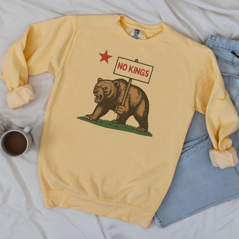 Yellow Comfort Colors sweatshirt flatlay with NO KINGS California bear graphic, paired with denim.
