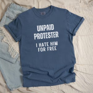Flat lay of faded blue Comfort Colors tee with white block protest text.