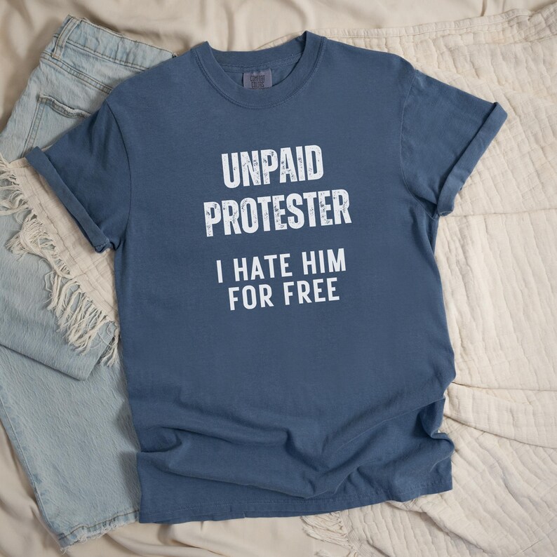Flat lay of faded blue Comfort Colors tee with white block protest text.