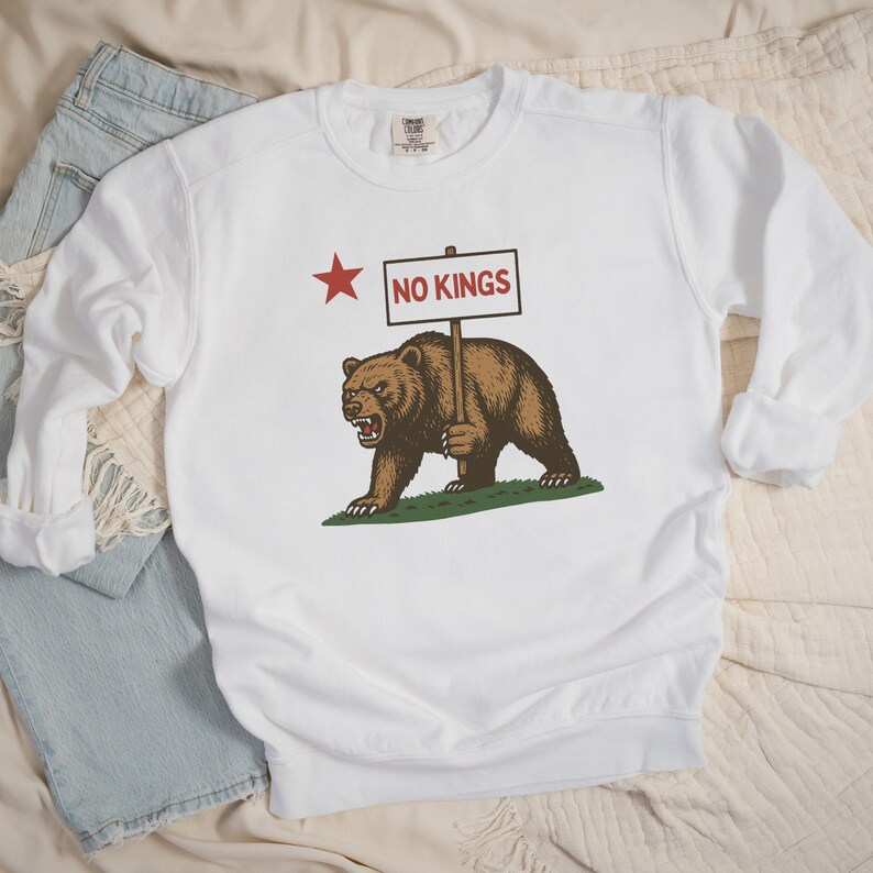 White Comfort Colors sweatshirt with California bear protest design holding a red RESIST sign.