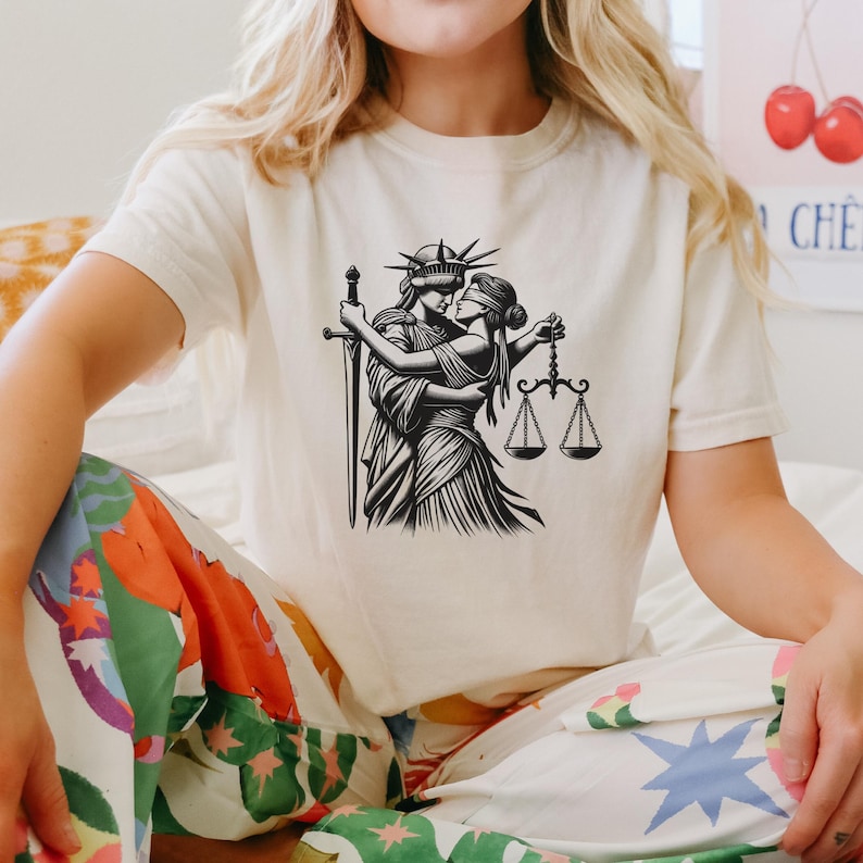 Natural beige shirt modeled seated, showing close-up of empowering queer justice artwork on Comfort Colors cropped fit