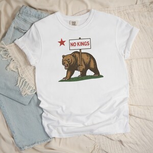White Comfort Colors tee flatlay with California resistance bear and NO KINGS sign graphic.
