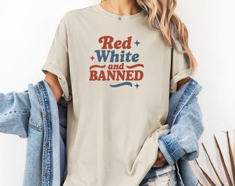 May include: Beige t-shirt with the text "Red White and Banned" in red and blue. The shirt has a relaxed fit and rolled-up sleeves. A denim jacket is draped over the shoulders.
