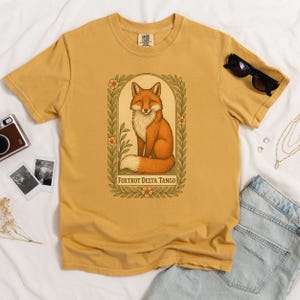 Mustard yellow Foxtrot Delta Tango Comfort Colors tee, illustrated fox and floral frame, subtle anti-Trump statement shirt.