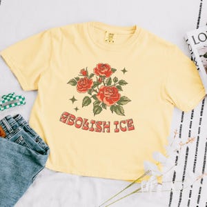 Yellow cropped tee with floral anti-ICE design styled flat lay with jeans and flowers
