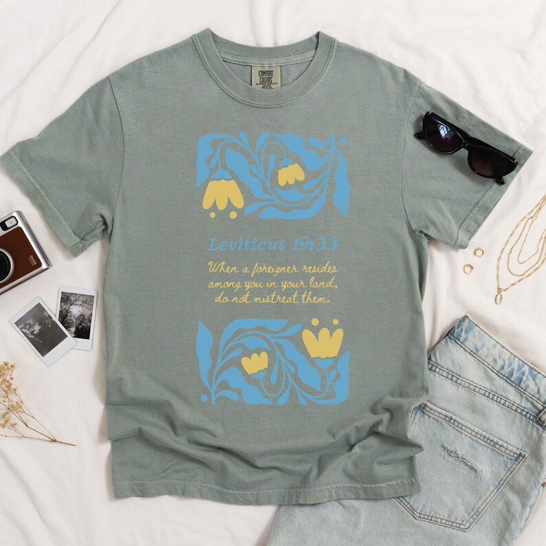 Bay green Comfort Colors T-shirt with retro Bible verse design reading “Do not mistreat them” and Matisse-style florals in yellow and blue