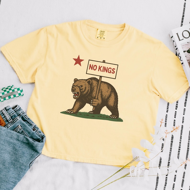 Yellow Comfort Colors cropped t-shirt with NO KINGS bear protest design, styled with book and accessories.