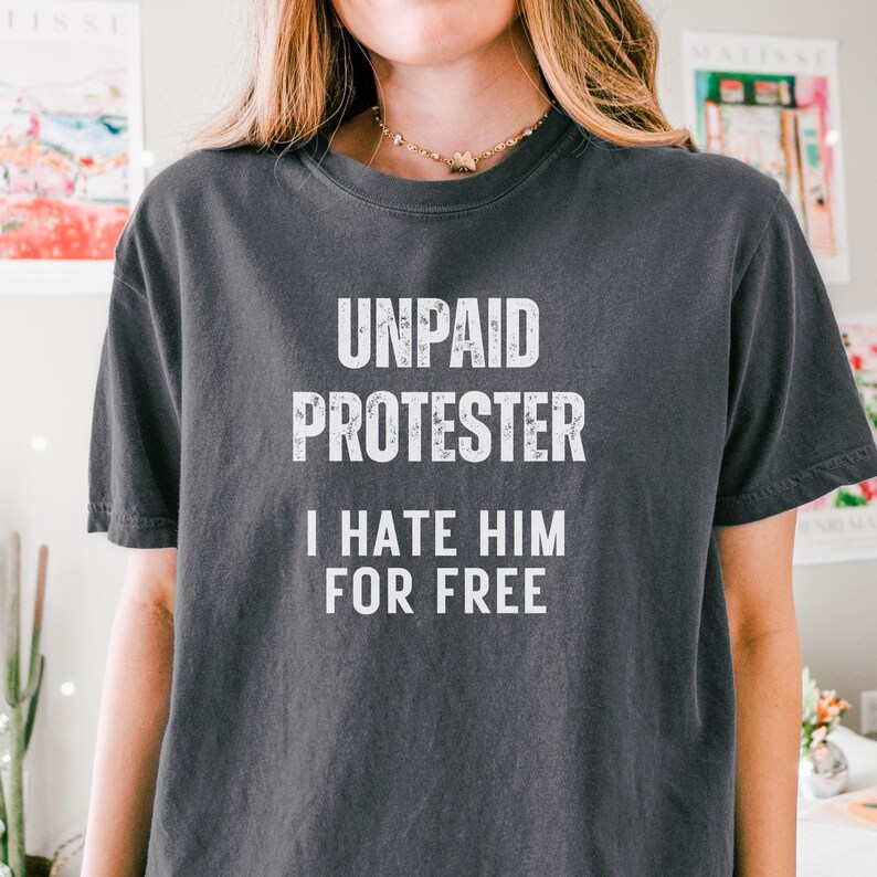 Model wearing vintage black tee with protest slogan “Unpaid Protester – I Hate Him For Free” styled with soft curls and layered necklace.