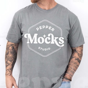 May include: A gray t-shirt with a white logo that says "Pepper Mocks Studio". The person wearing the shirt has tattoos on their arms.