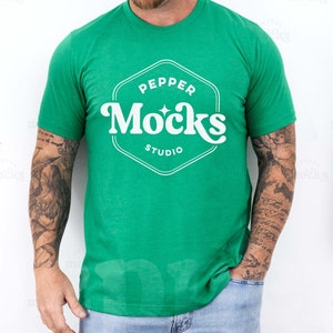 May include: A green t-shirt with a white logo that says "Pepper Mocks Studio". The person wearing the shirt has tattoos on their arms.