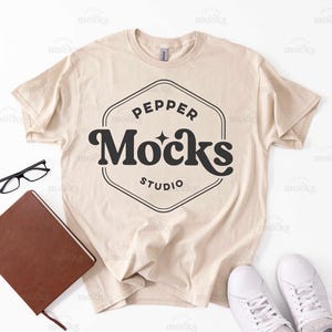 May include: A beige t-shirt with a black graphic design that says "Pepper Mocks Studio" in a retro font.