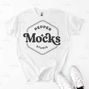 Op de afbeelding: Wit T-shirt met een zwart-wit logo met de tekst "Pepper Mocks Studio".