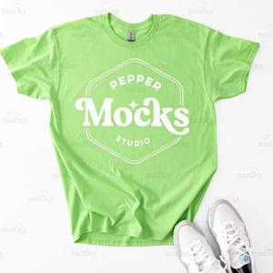 Könnte beinhalten: Ein leuchtend grünes T-Shirt mit einem weißen Logo, auf dem in einer Retro-Schrift "Pepper Mocks Studio" steht.