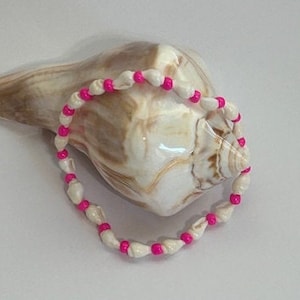 May include: A white and pink shell bead bracelet. The bracelet is made of small white shells with pink beads in between.