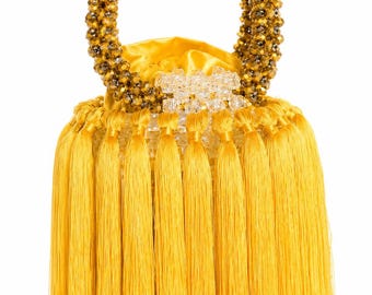 May include: A bucket-style handbag featuring a circular handle made of faceted bronze-colored beads. The body of the bag is covered in long, vibrant yellow silk-like tassels that hang from a clear acrylic frame with a yellow satin drawstring closure.
