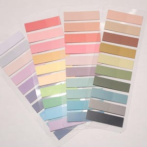 May include: Three clear plastic sheets holding multiple rectangular adhesive page markers in a variety of pastel and muted tones. The colors include shades of pink, orange, yellow, green, blue, purple, brown, gray, and black arranged in rows.