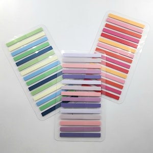 May include: Three clear plastic sheets containing multiple rows of thin, rectangular adhesive page markers. The markers are arranged in various color palettes, including shades of green, blue, yellow, pink, red, purple, and neutral gray tones.