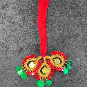May include: A red tassel hangs from a gold and red beaded ornament with green accents.
