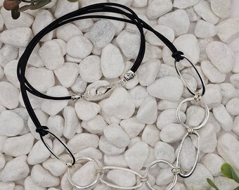 May include: A black cord necklace with a silver chain and multiple oval-shaped silver links. The necklace is photographed on a white background.