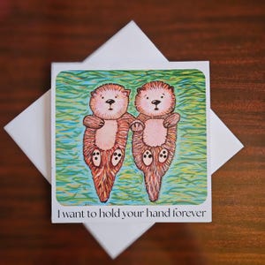 Tarjeta de felicitación "Te amo" con nutrias tomadas de la mano. "Quiero tomarte de la mano para siempre".