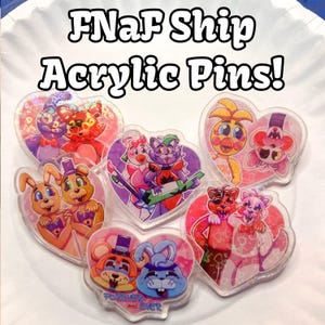 Può includere: Sei spille in acrilico a forma di cuore che rappresentano diverse coppie del franchise FNaF. Le spille sono olografiche e hanno una finitura scintillante. Il testo "FNaF Ship Acrylic Pins!" è scritto in grandi lettere bianche nella parte superiore dell'immagine.
