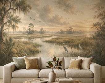 May include: A beige sofa with velvet pillows sits before a wall mural depicting a marsh landscape with trees, birds, and a winding river. A round wooden coffee table with a natural edge holds a ceramic vase with green leaves and two books.