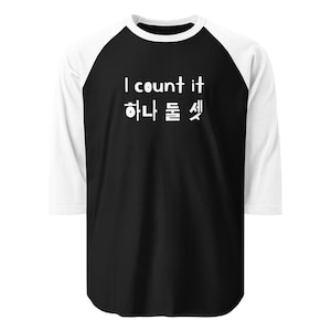 May include: Black and white raglan baseball tee with the text "I count it" in English and Korean. The shirt has white sleeves and a black body.