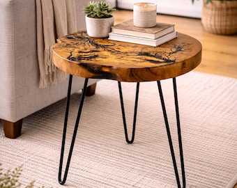 May include: A round wooden side table with a unique, natural wood grain pattern. The table has black hairpin legs and is topped with a small potted plant, books, and a candle. The table is approximately 20 inches in diameter.