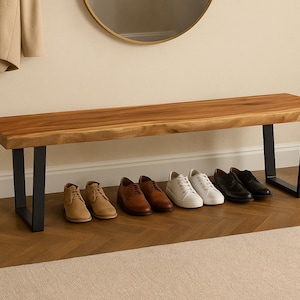May include: A wooden bench with a natural finish and black metal legs. Various pairs of shoes in brown, tan, and black are lined up below the bench. A round mirror hangs on the wall above.