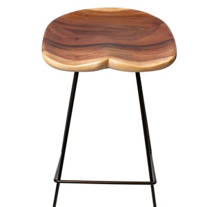 Puede incluir: Un taburete de bar de madera con asiento de madera natural y patas de metal negro. El asiento tiene una forma org&aacute;nica &uacute;nica y un color marr&oacute;n intenso. Las patas del taburete son delgadas e inclinadas, proporcionando una est&eacute;tica moderna.