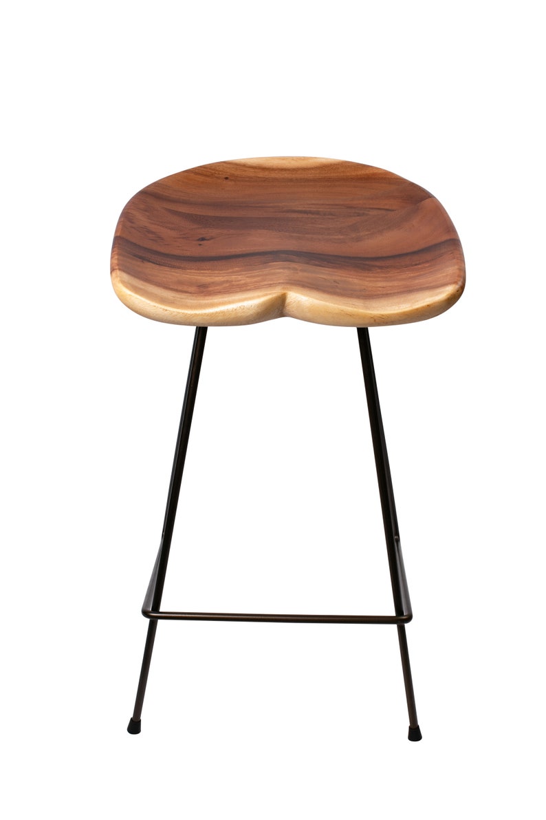 Puede incluir: Un taburete de bar de madera con asiento de madera natural y patas de metal negro. El asiento tiene una forma org&aacute;nica &uacute;nica y un color marr&oacute;n intenso. Las patas del taburete son delgadas e inclinadas, proporcionando una est&eacute;tica moderna.