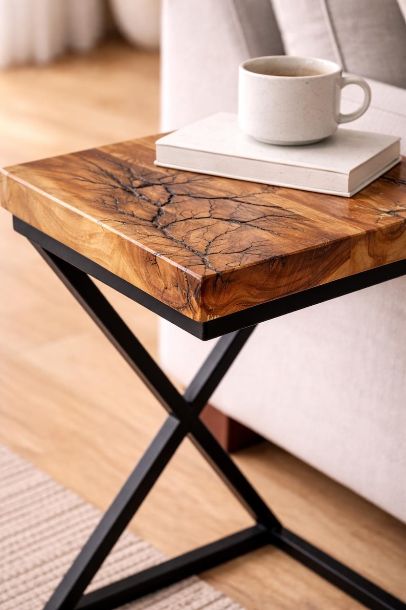 May include: A small, square side table with a unique wood grain top and black metal legs. The tabletop features a striking, natural pattern. A white book and a ceramic mug sit on top of the table. The table is approximately 20 inches wide.