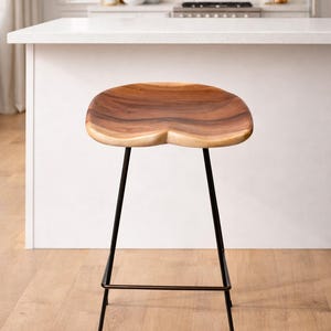Puede incluir: Un taburete de bar de madera con asiento contorneado y patas de metal negro. El asiento es de madera natural con un patr&oacute;n de vetas &uacute;nico. El taburete est&aacute; dise&ntilde;ado para uso en cocina o bar.