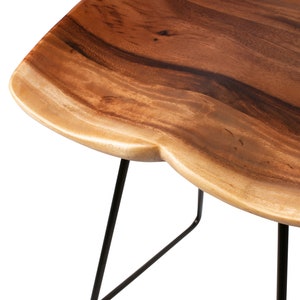Puede incluir: Taburete de bar de madera con asiento de borde vivo y patas de metal negro. El asiento es de madera natural con un acabado marr&oacute;n claro y una forma &uacute;nica. Las patas son finas e inclinadas, proporcionando estabilidad.