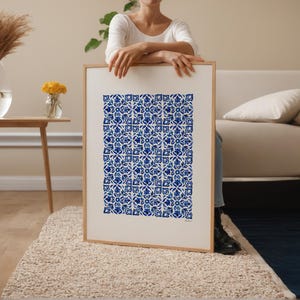 以下が含まれることがあります： 青と白の花柄が繰り返される額入りのプリント。アートワークは人が持っており、フレームは明るい木の色です。プリントは、ニュートラルな色調の部屋、ソファ、ラグに展示されています。