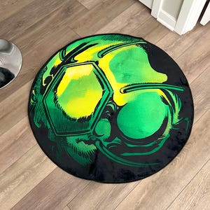 Peut inclure: Tapis rond avec un motif de ballon de football. Le tapis présente un fond noir avec un graphisme de ballon de football vert et jaune. Le tapis est posé sur un sol en bois.
