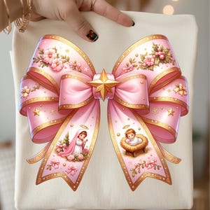 Puede incluir: Un bolso tote crema con un gran lazo rosa con ribetes dorados y detalles florales. Una estrella dorada adorna el centro del lazo. Las colas del lazo muestran ilustraciones de la Virgen María y el niño Jesús. Diseño festivo y navideño.