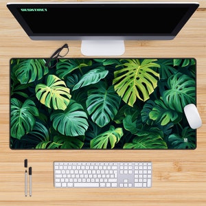 May include: A green and black desk mat with a tropical leaf pattern. The mat is on a wooden surface with a computer monitor, keyboard, and mouse.
