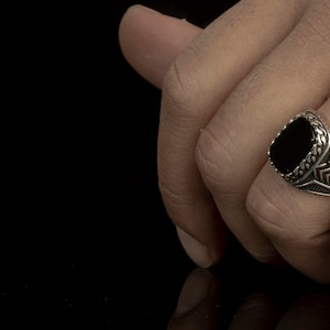 May include: A silver ring with a black oval gemstone set in a detailed design.