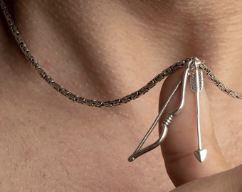 May include: A silver chain necklace with a silver bow and arrow pendant.