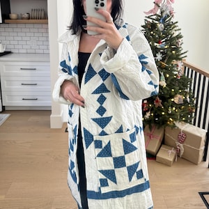 Peut inclure: Une veste matelassée blanche avec un motif géométrique bleu. La veste a un col et une fermeture à boutons. La veste est à manches longues et a une poche plaquée sur le côté gauche.